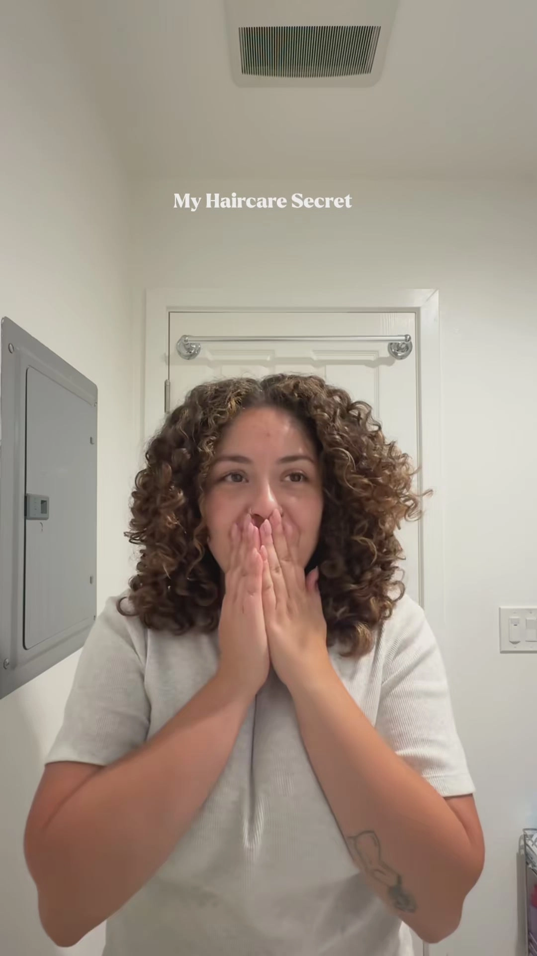Still from a customer video: a woman with curly hair, hands over her mouth