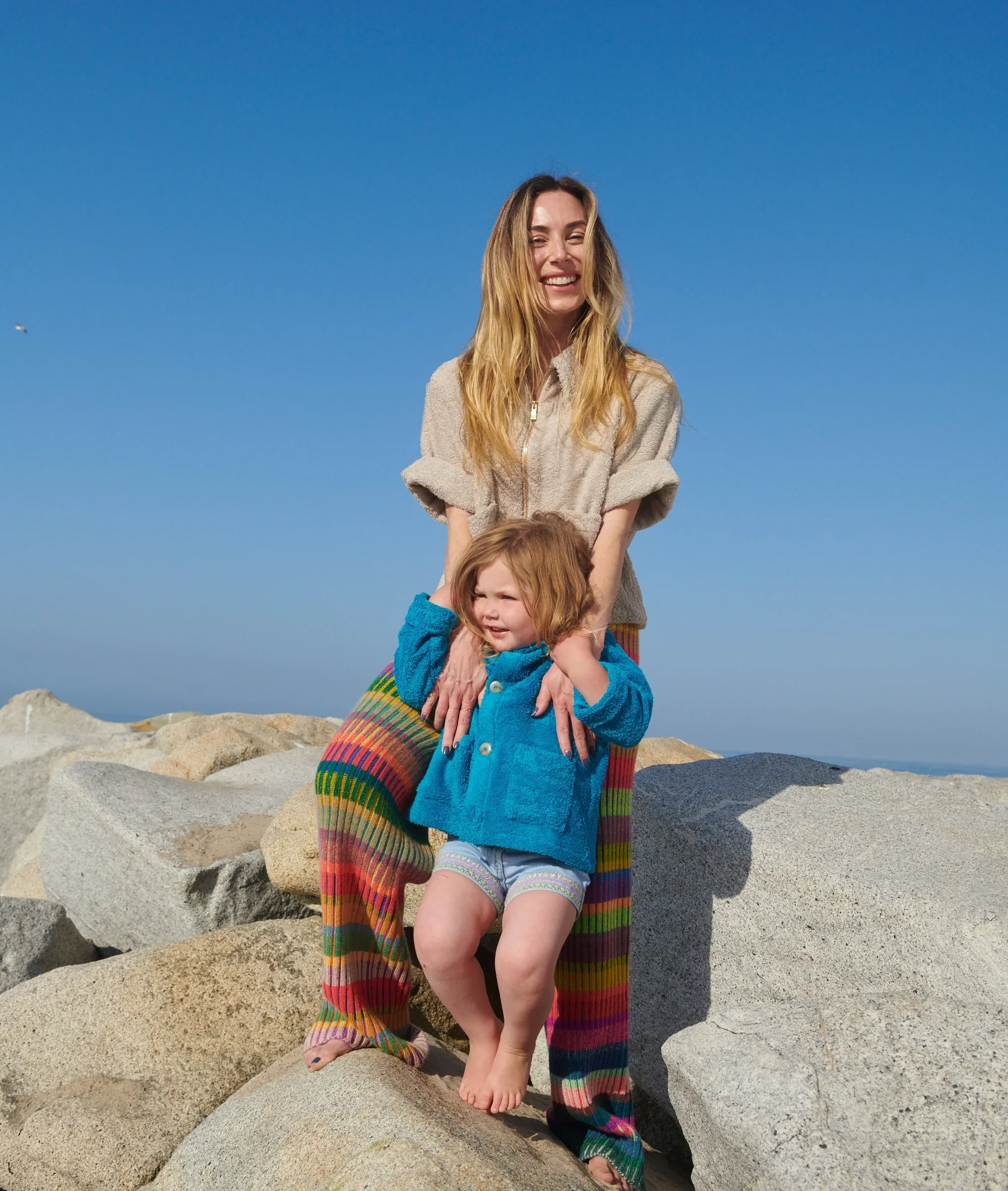 A woman and a child sitting together on coastal rocks